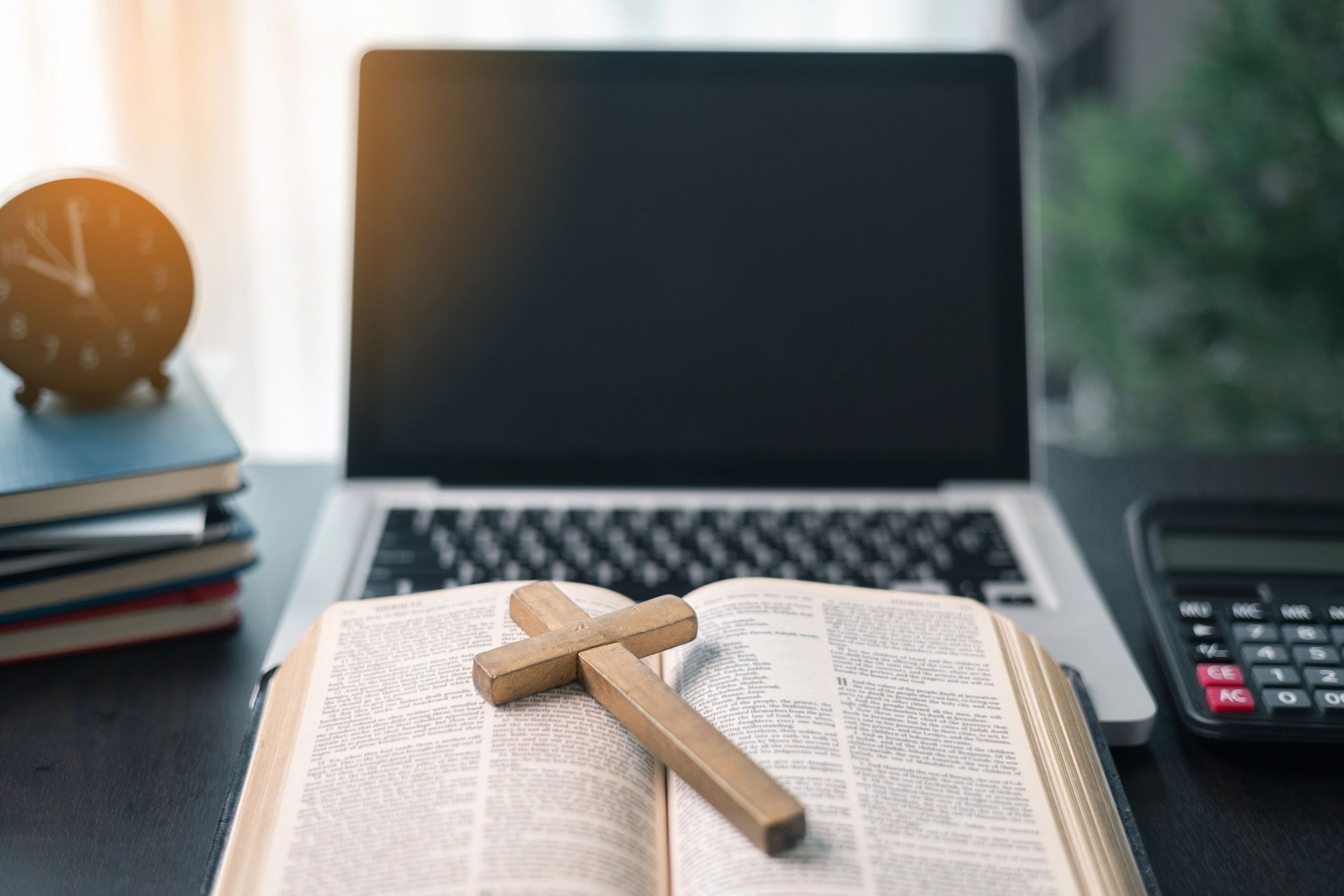 Cross resting on a Bible near a laptop